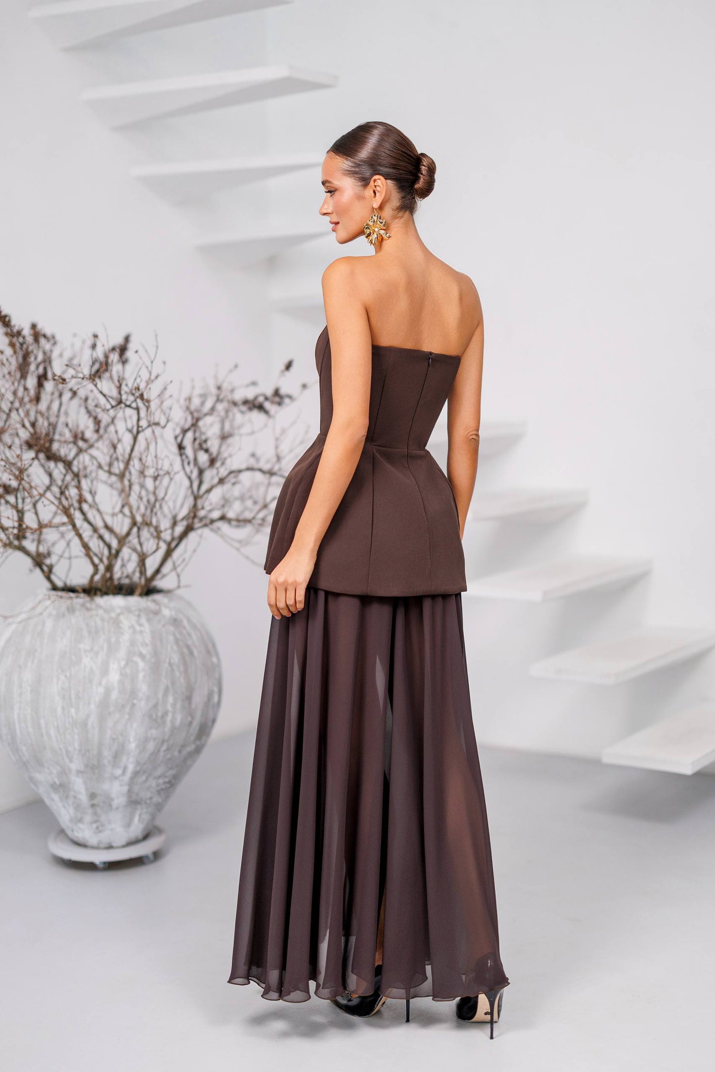 Woman wearing a brown strapless gown standing in front of a white abstract sculpture.