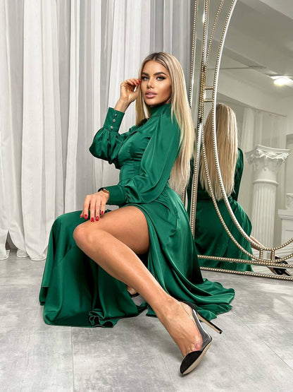 Woman in a green dress sitting in front of a mirror in a room with white curtains.