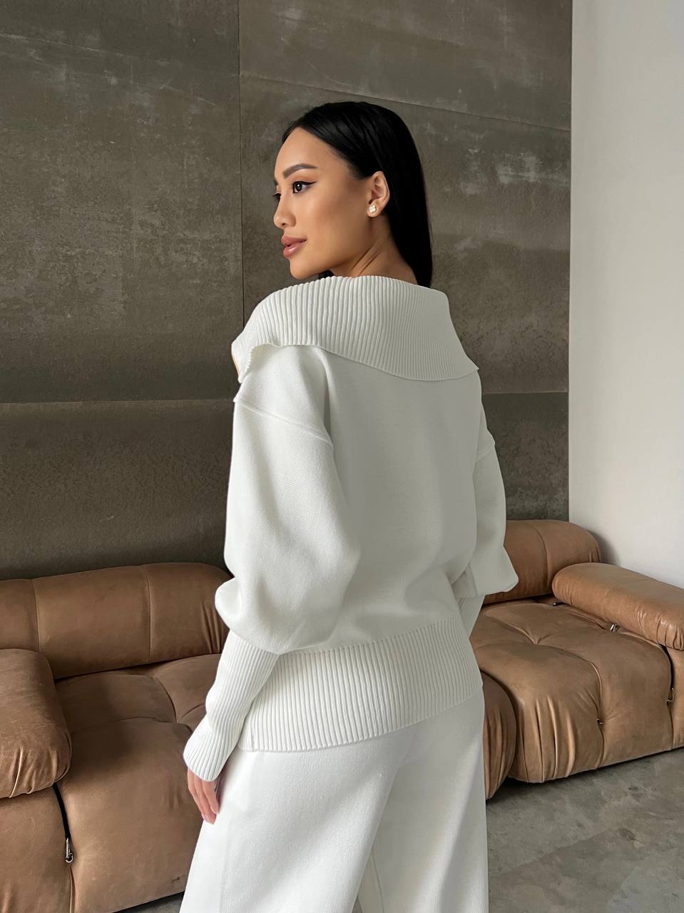 Woman in a white outfit standing in a room with brown sofas.