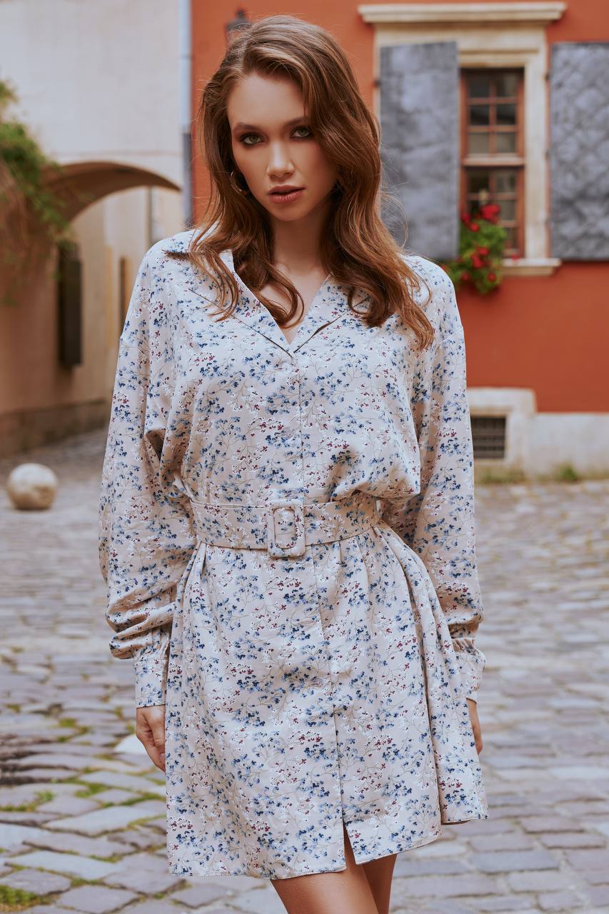 Woman wearing a floral dress standing on a cobblestone street with a building in the background.