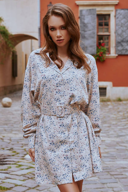 Woman wearing a floral dress standing on a cobblestone street with a building in the background.