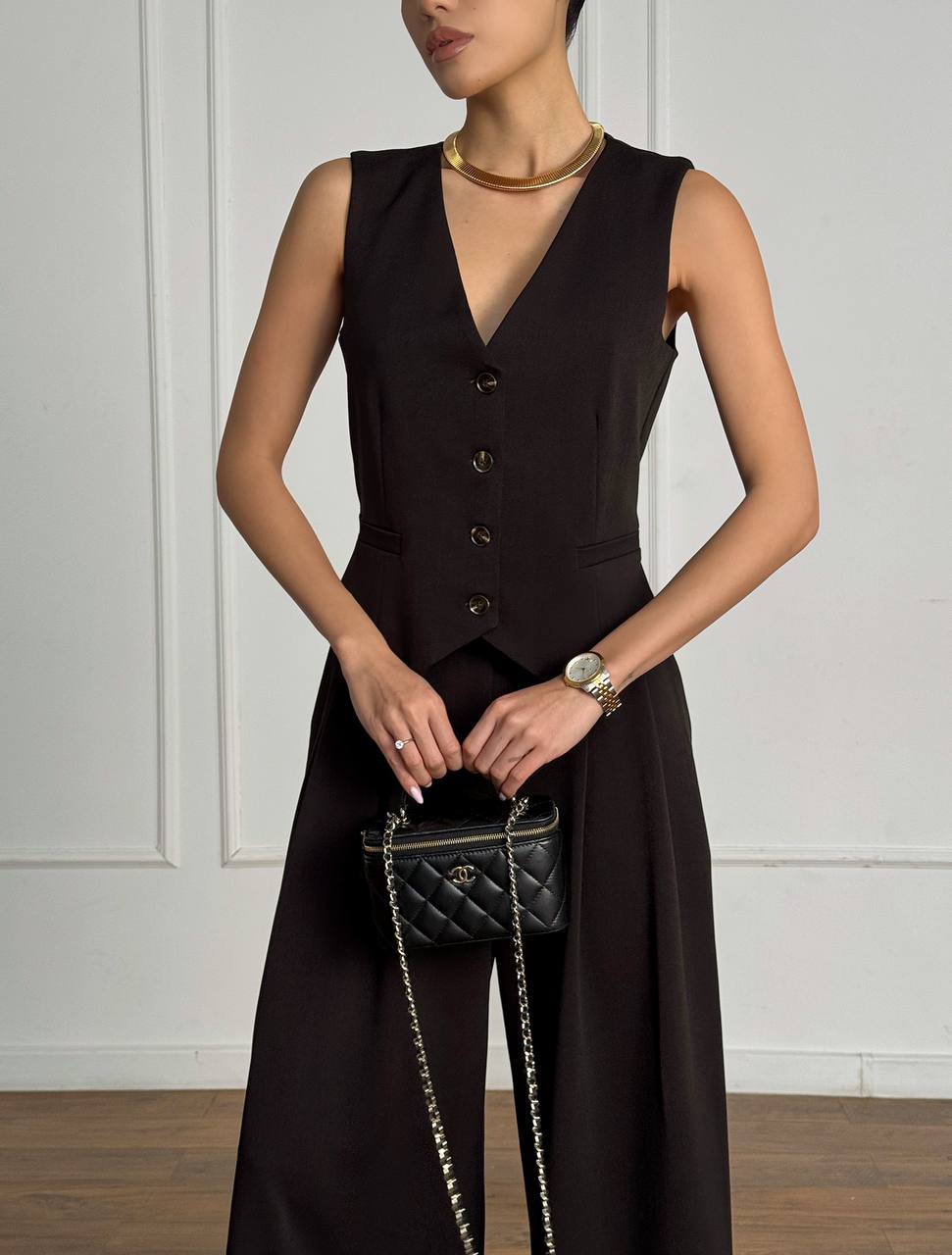 Woman wearing a black sleeveless dress with a vest, holding a black handbag.