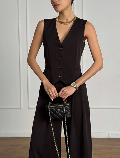 Woman wearing a black sleeveless dress with a vest, holding a black handbag.