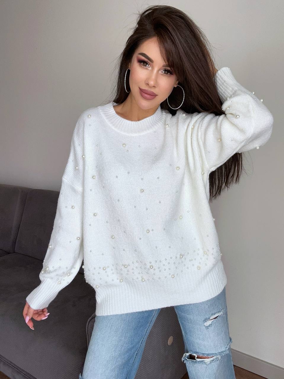 Woman wearing a white sweater with pearl embellishments in a casual setting.