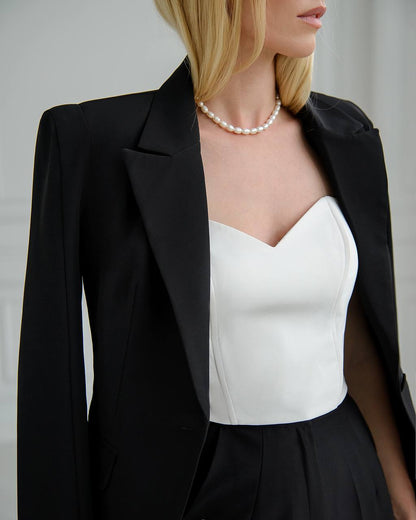 Person wearing a black blazer over a white top with a pearl necklace against a neutral background