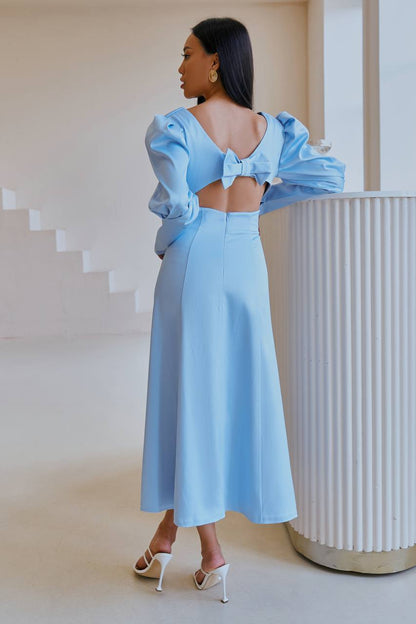 Woman in a light blue outfit with a bow detail standing in a minimalistic setting.