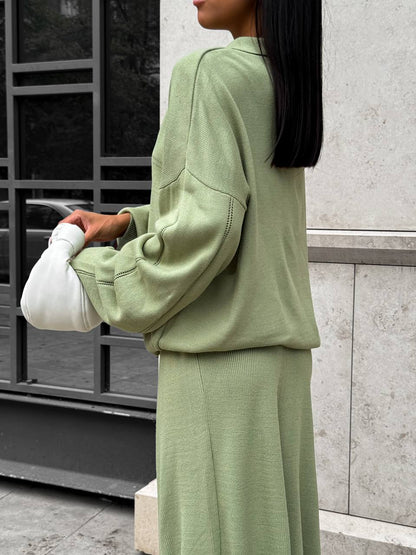 Person wearing a light green outfit with a cast on their arm, standing against a building.