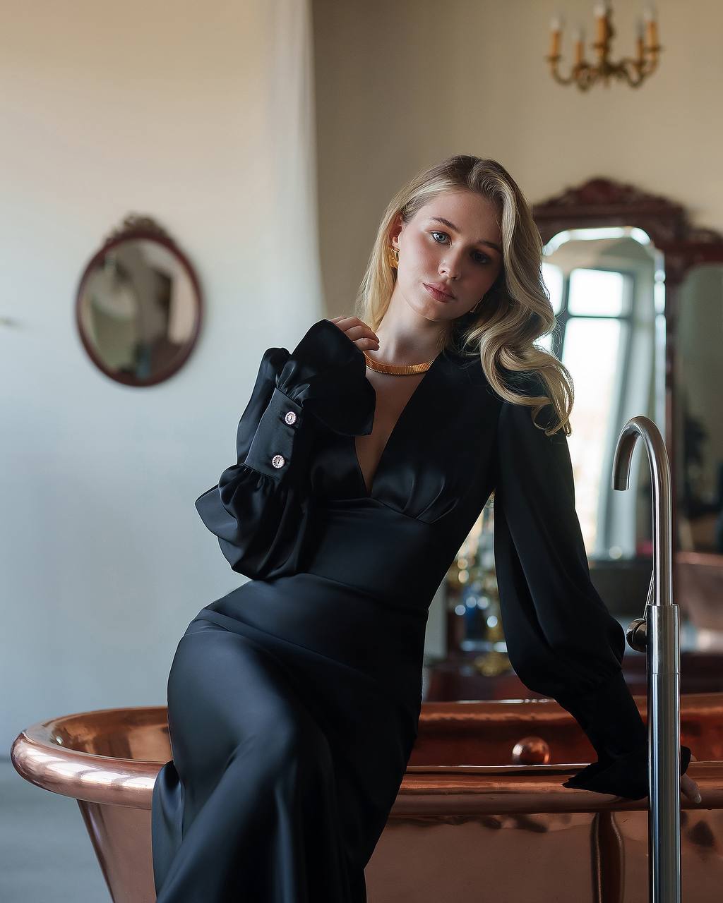 Woman in a black outfit sitting on a copper bathtub in an elegant room.