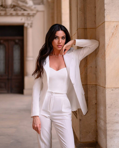 Woman in a white suit standing against a stone wall.