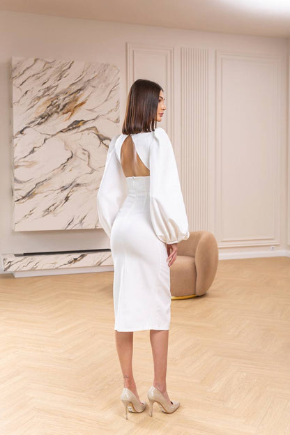 Woman in a white dress standing in a room with a marble wall art piece.
