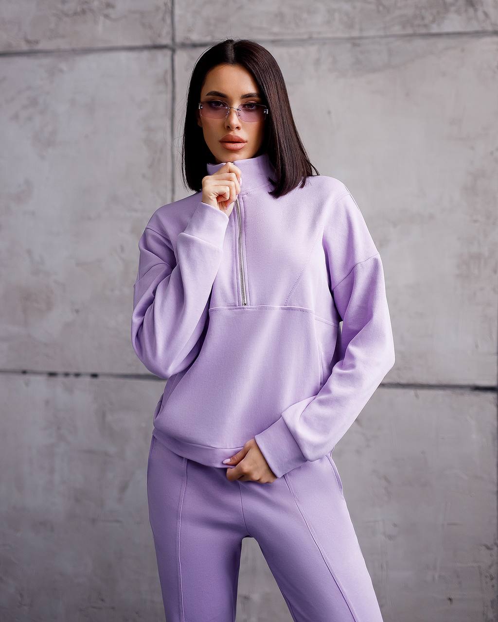 Woman wearing a light purple tracksuit against a gray concrete wall