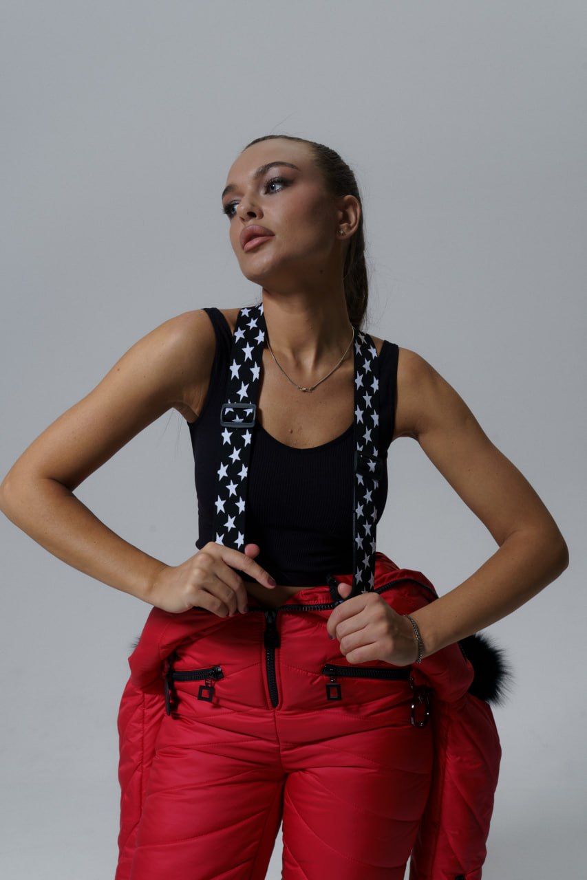 Woman wearing a black tank top with star patterns and red pants against a gray background