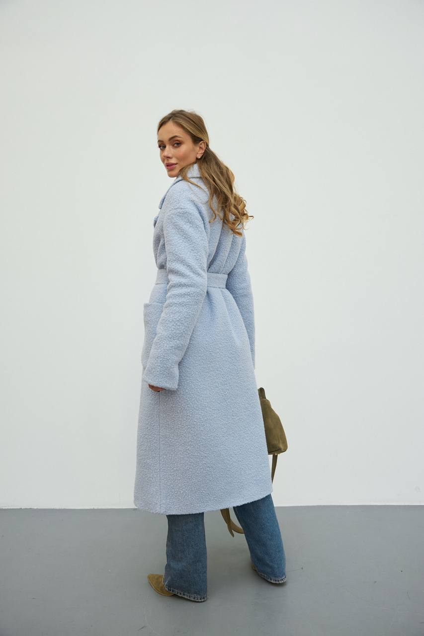 Woman wearing a long light blue coat against a white background