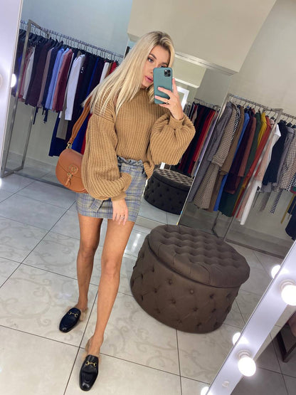 Woman taking a mirror selfie in a clothing store, wearing a brown ribbed sweater and plaid skirt.