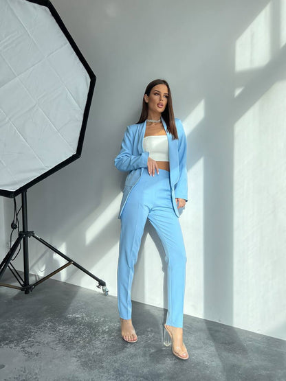Woman in a light blue suit standing in a studio setting with photography equipment.