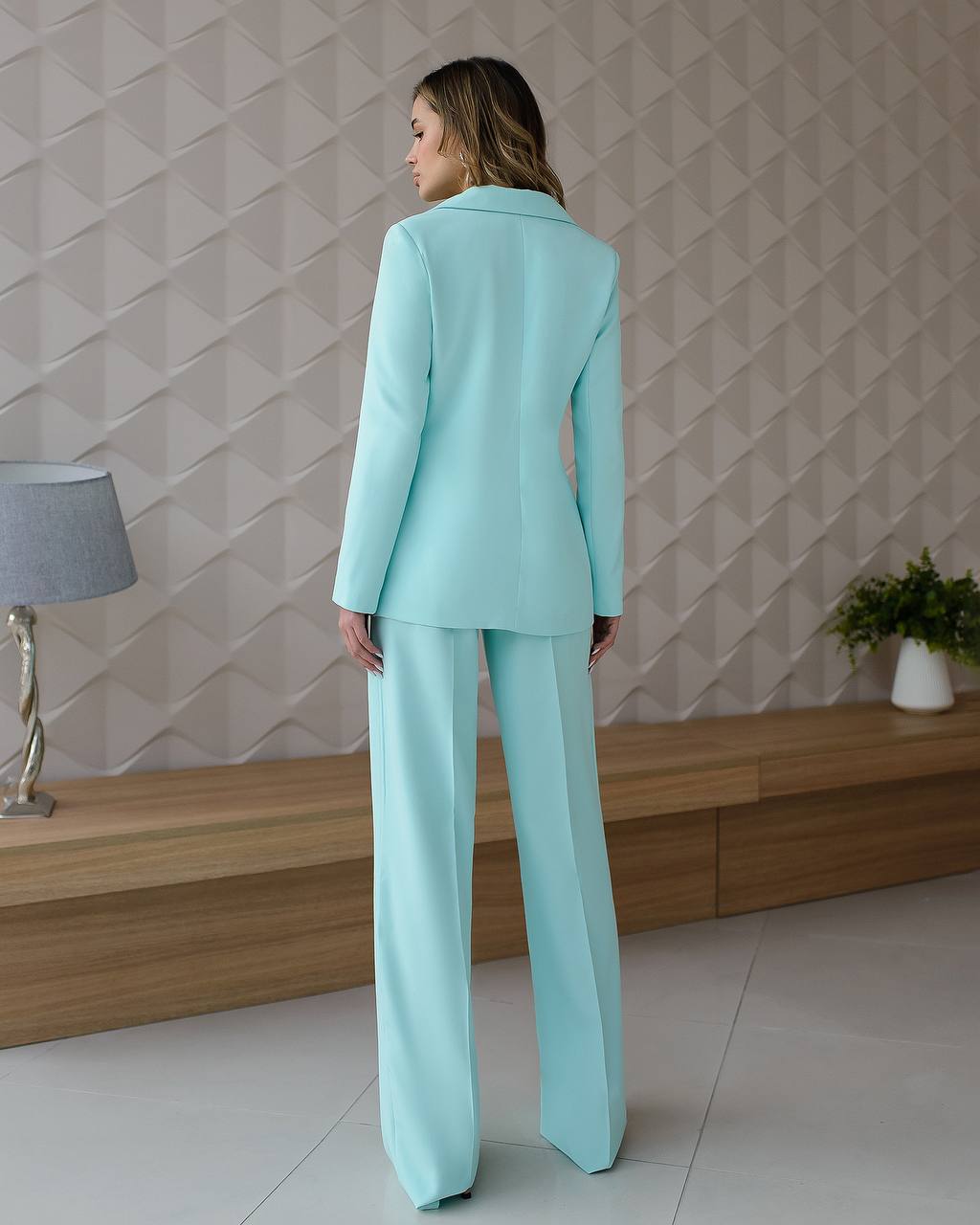 Woman wearing a light blue suit standing in a room with a geometric wall pattern.