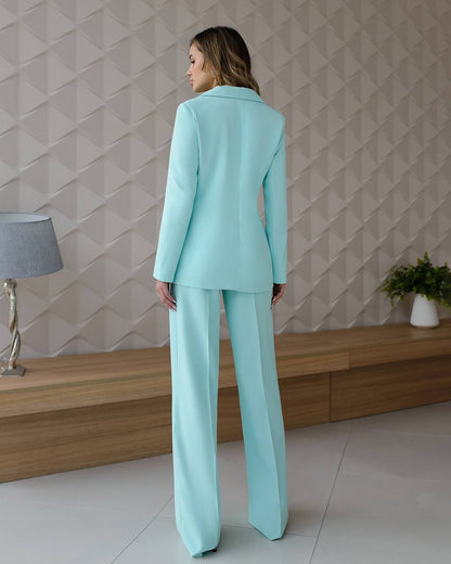 Woman wearing a light blue suit standing in a room with a geometric wall pattern.