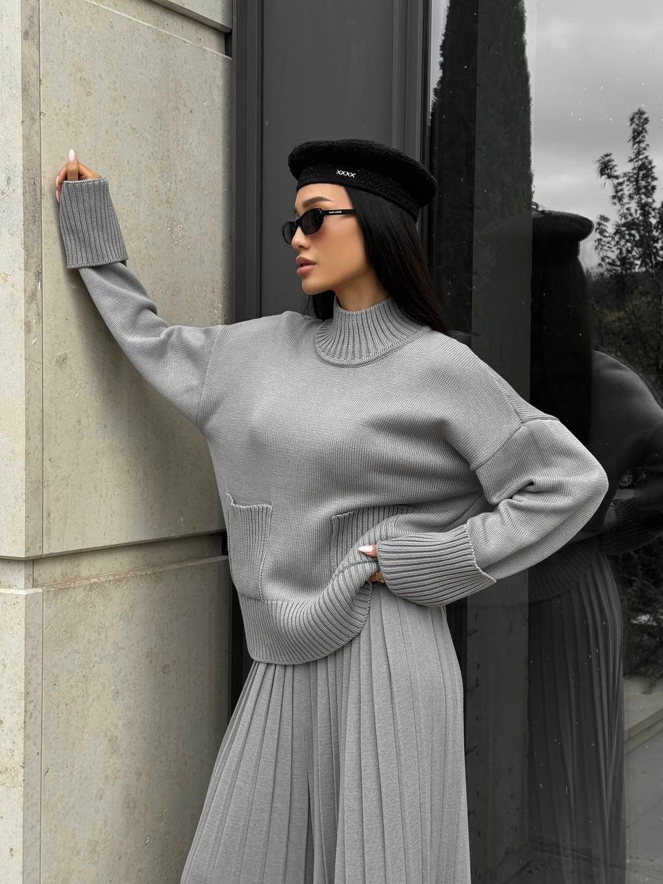 Woman in a gray outfit standing against a building