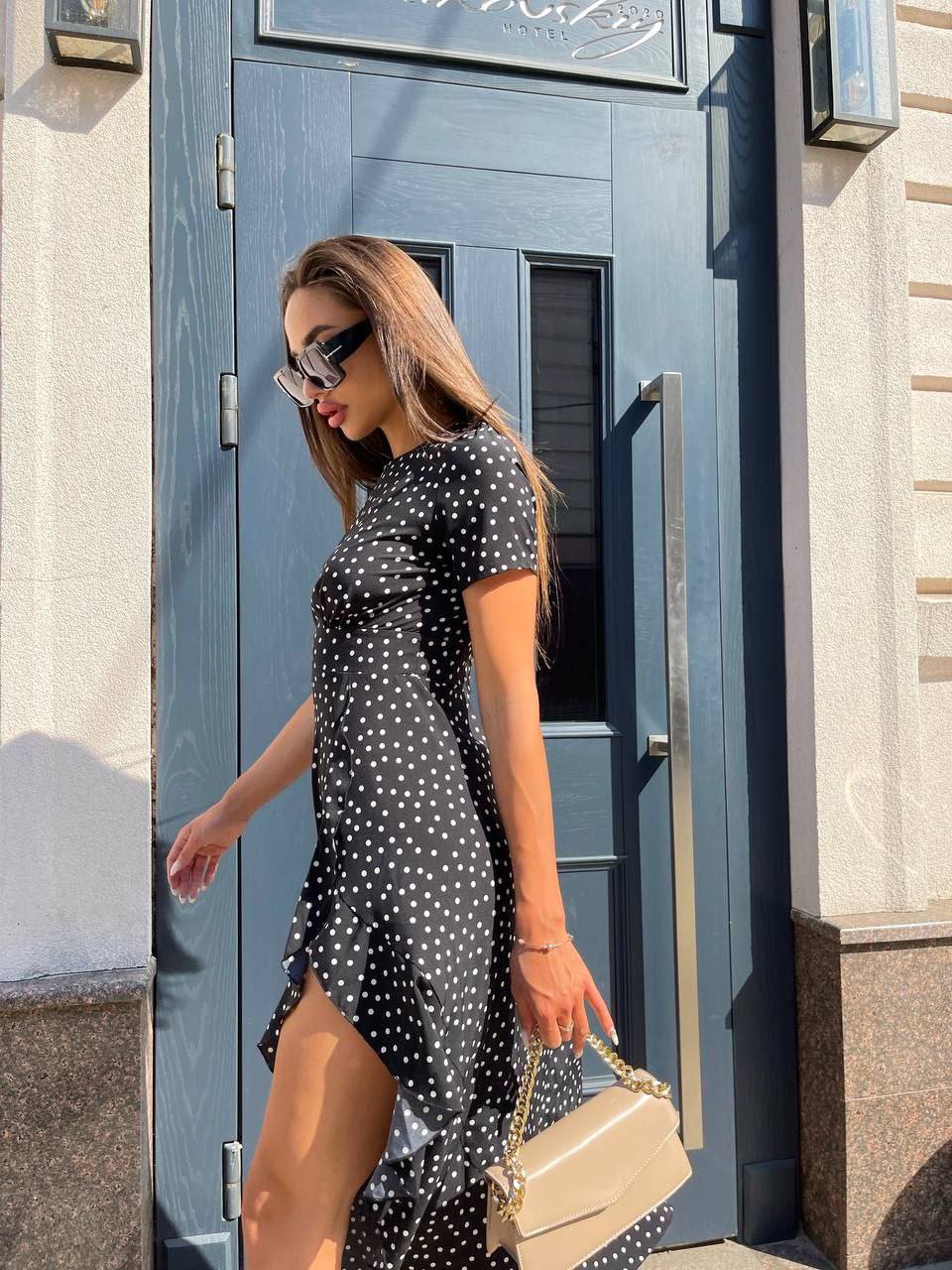Woman in a black polka dot dress standing in front of a blue door.