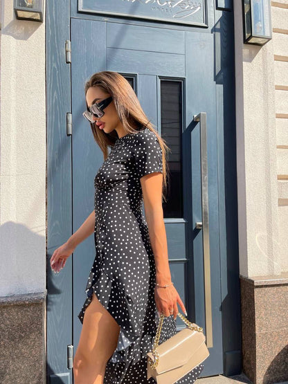 Woman in a black polka dot dress standing in front of a blue door.