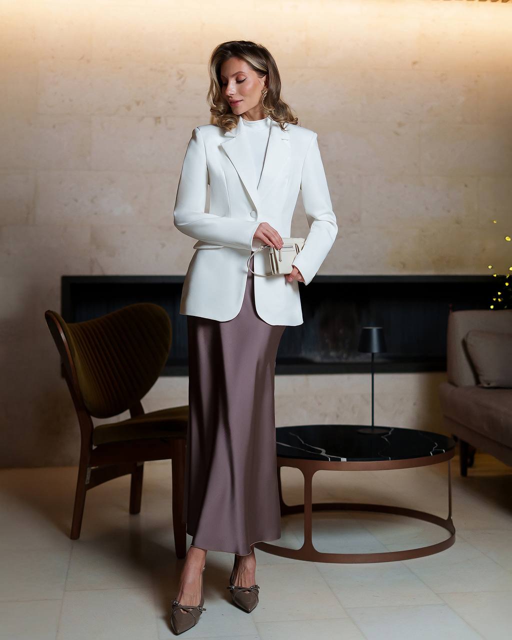 Woman in a white blazer and purple skirt standing in an indoor setting.