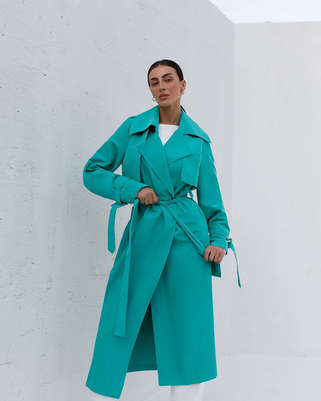 Woman wearing a teal coat against a white background