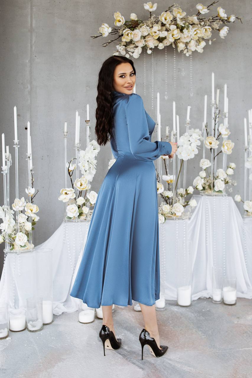 Woman in a blue dress standing in front of floral arrangements and candles.