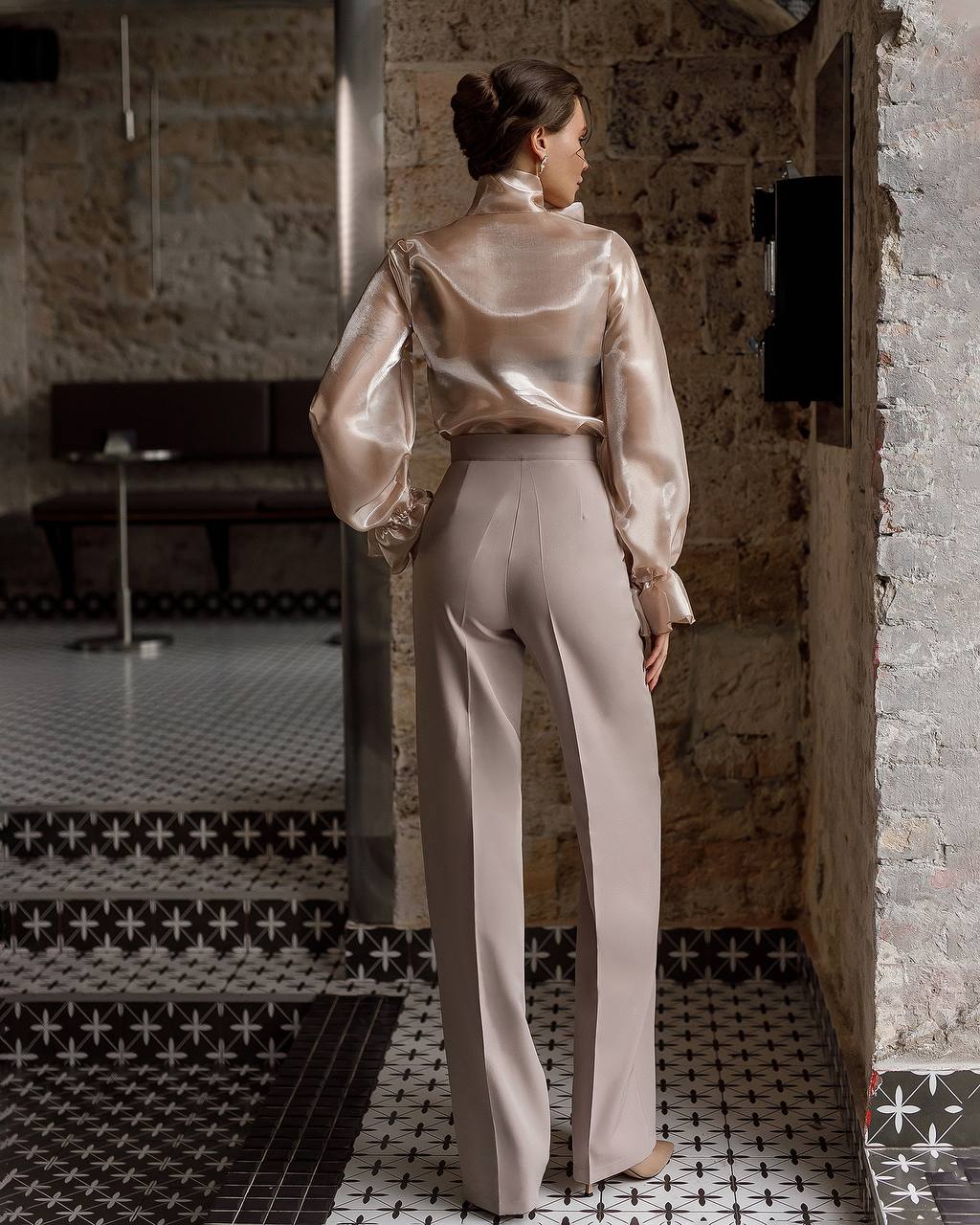 Woman in a beige satin outfit standing in a room with patterned tiles.