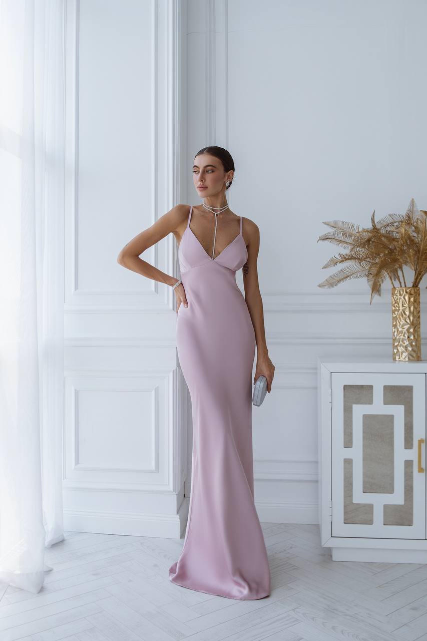 Woman in a pink evening gown standing in a stylish room with decorative elements.