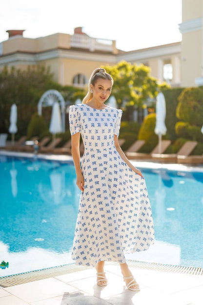 Woman in a white dress with blue patterns standing by a pool