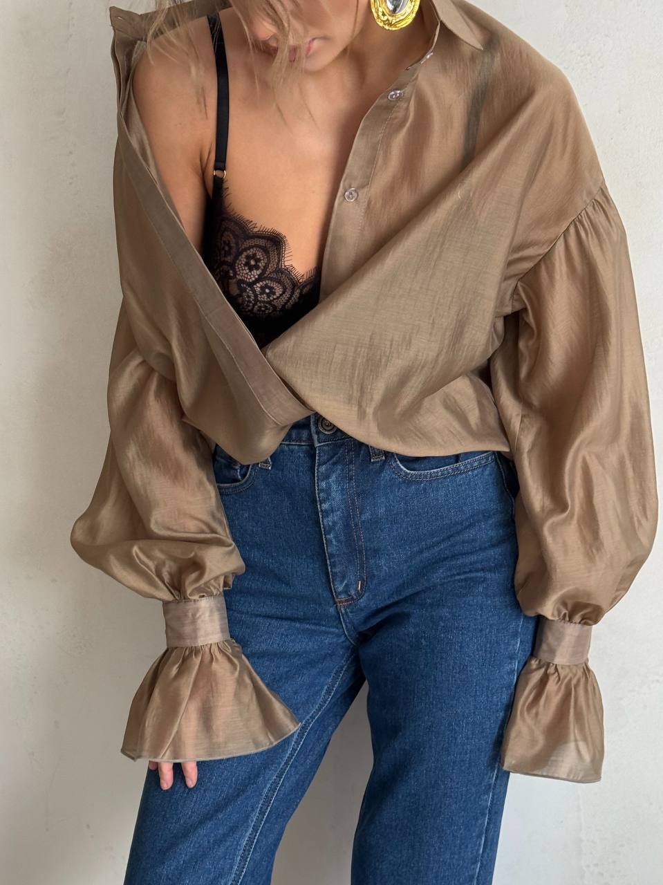 Person wearing a beige blouse with puffed sleeves and blue jeans against a plain background