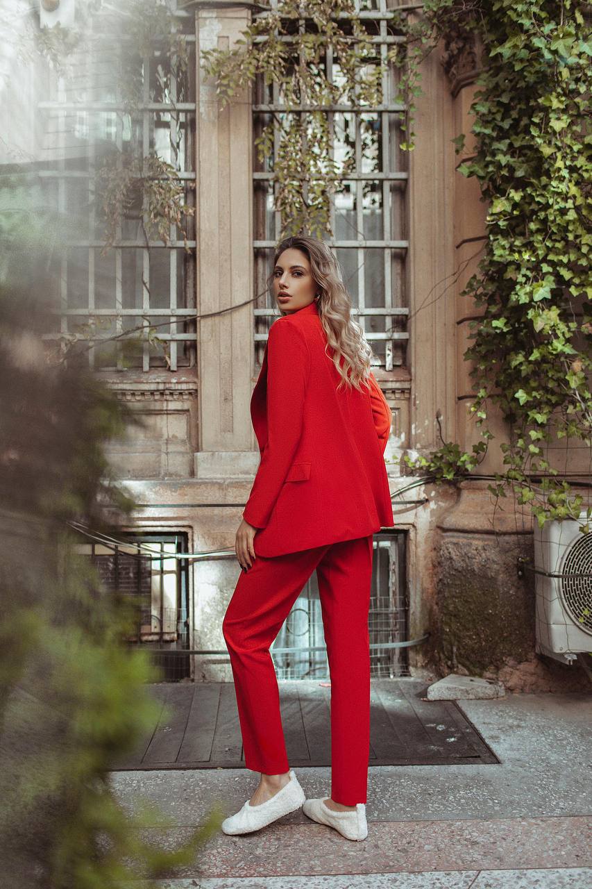 Woman in a red suit standing in an urban setting with greenery.