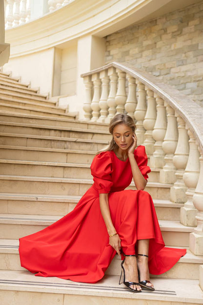 Woman in a red dress sitting on a staircase with classical architecture.