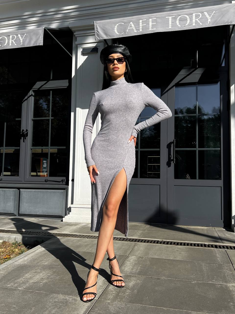 Woman in a gray dress standing in front of a building with 'Cafe Tory' sign.