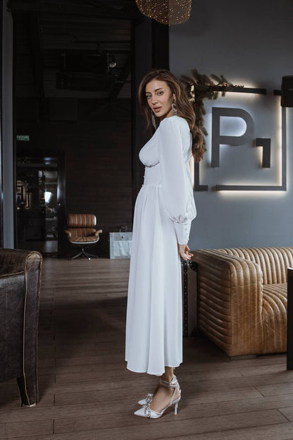 Woman in a white dress standing in a stylish interior setting with a 'P' logo on the wall.
