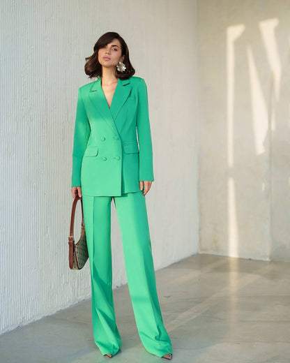 Woman wearing a green suit standing against a light-colored wall.
