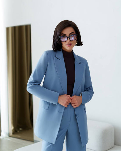 Woman wearing a light blue suit and glasses indoors.