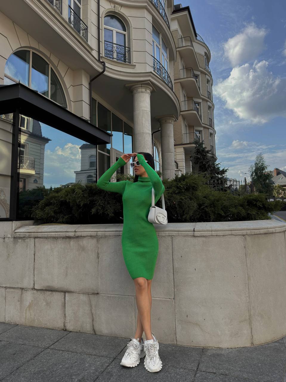 Woman in a green dress standing in front of a building with a white car in the background