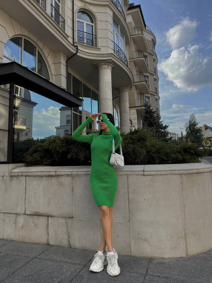 Woman in a green dress standing in front of a building with a white car in the background