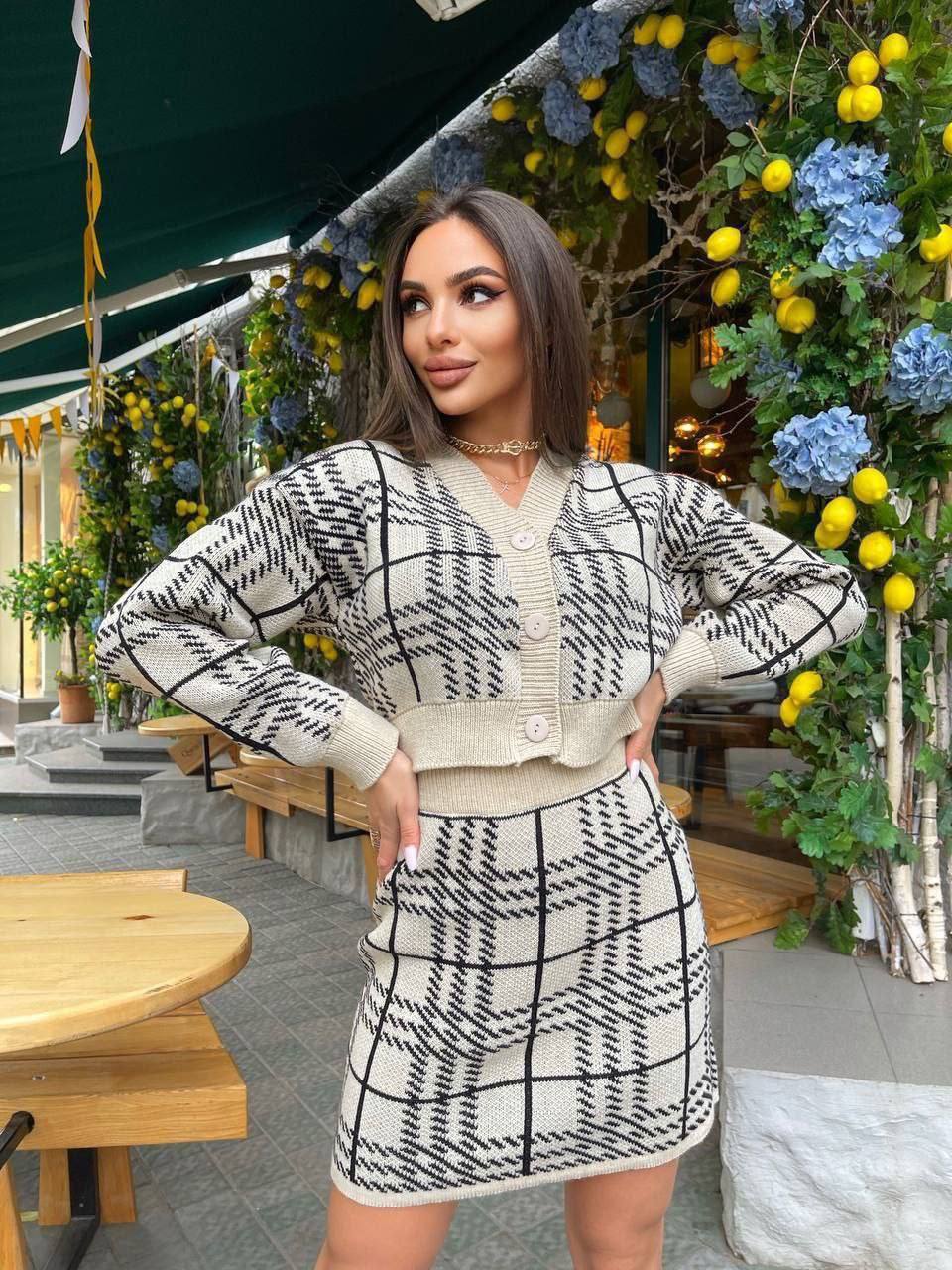 Woman wearing a black and white patterned outfit standing in front of floral decorations.