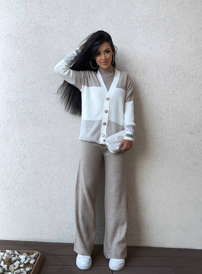 Woman wearing a two-tone cardigan and beige pants against a plain wall.