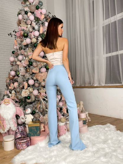 Woman in light blue pants and beige top standing in front of a decorated Christmas tree.