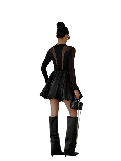 Person wearing a black dress with sheer panels and black knee-high boots on a white background