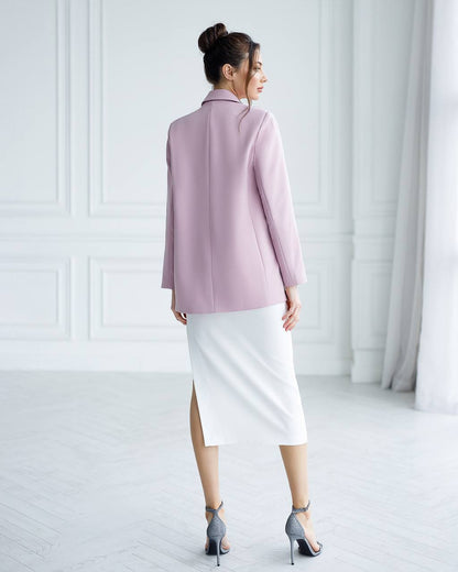 A woman is shown from the back wearing a lavender long-sleeve blazer and a white midi skirt, paired with gray high-heeled sandals, in a bright white room with classic paneled walls.