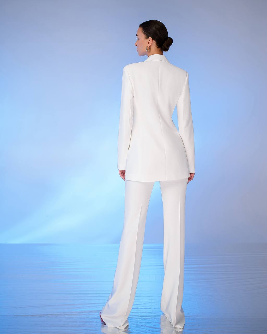 Person wearing a white suit standing against a gradient blue background
