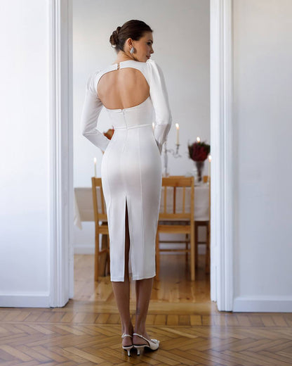 Woman in a white dress standing in a room with wooden flooring and white walls.