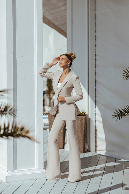 Woman in a beige suit standing in a sunlit room with white walls and wooden floor.