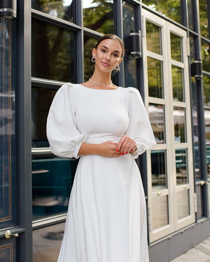 Woman in a white dress standing in front of a building with large windows.