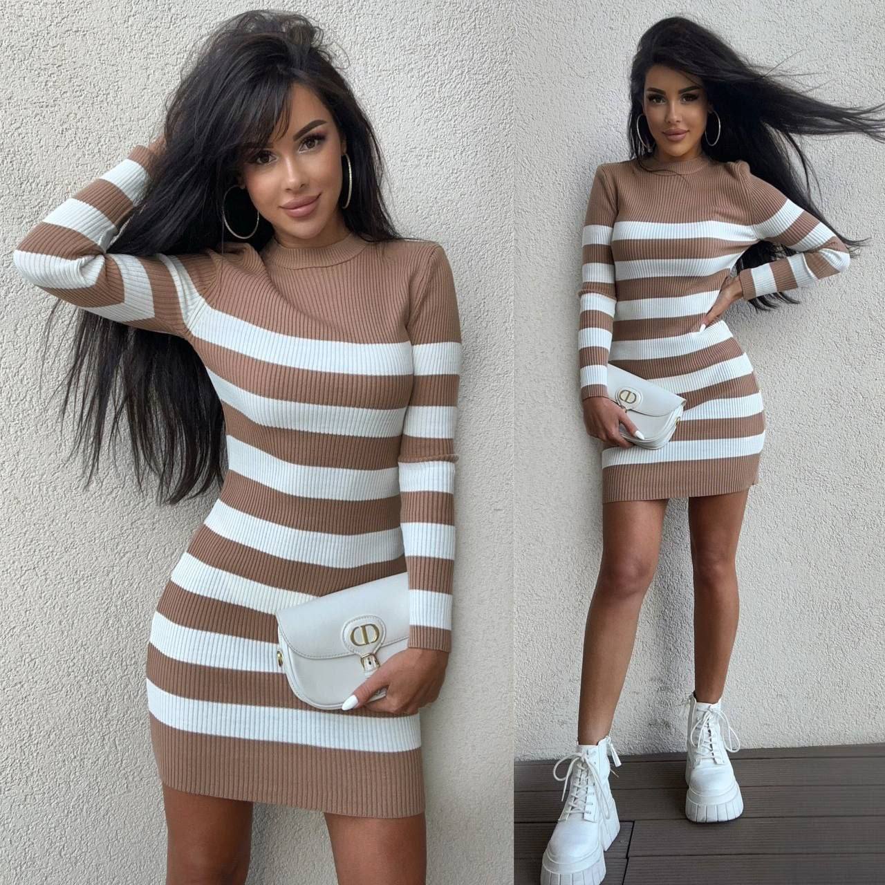 Woman wearing a brown and white striped dress against a plain wall.