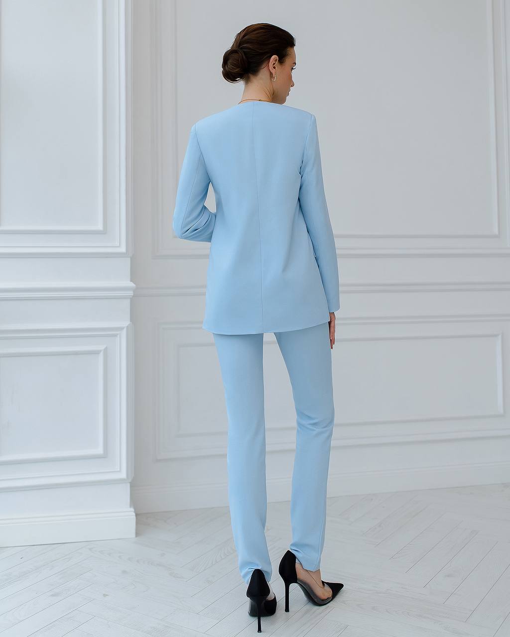Woman wearing a light blue suit standing against a white paneled wall.